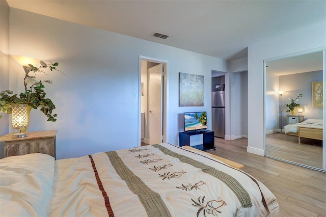 bedroom with freestanding refrigerator, wood finished floors, visible vents, and baseboards