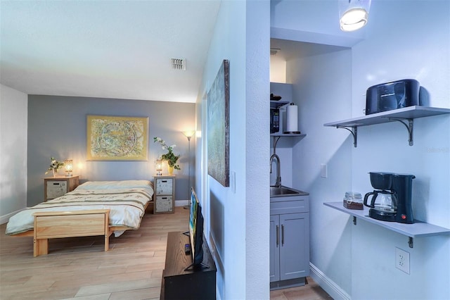 bedroom featuring light wood-style floors, visible vents, a sink, and baseboards