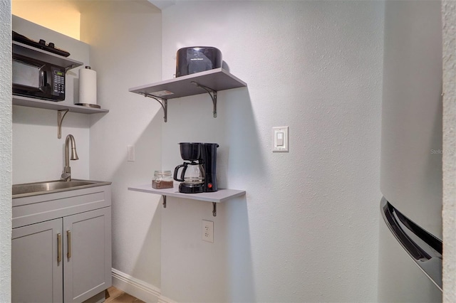 kitchen with black microwave, baseboards, open shelves, and a sink