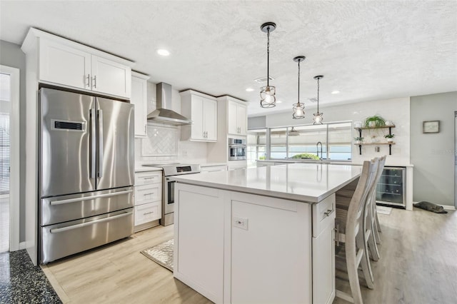 kitchen featuring white cabinets, light wood-style floors, wine cooler, stainless steel appliances, and wall chimney range hood