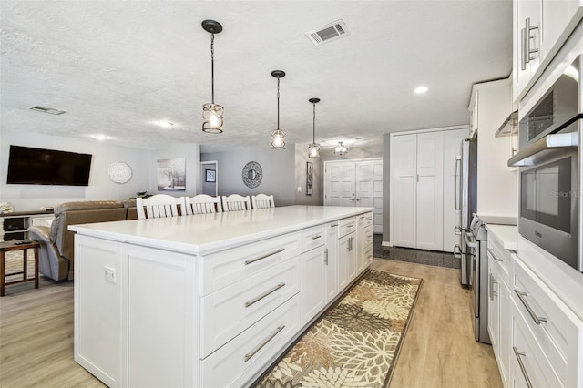 kitchen with white cabinets, light wood finished floors, visible vents, and a center island