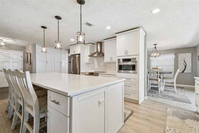 kitchen with stainless steel appliances, white cabinetry, light countertops, wall chimney range hood, and a center island