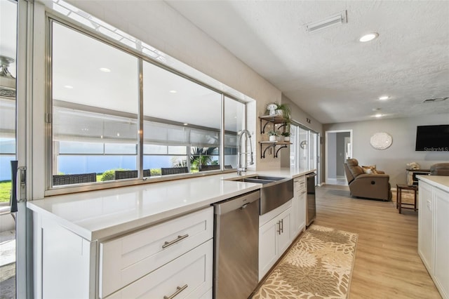 kitchen with dishwasher, open floor plan, light countertops, white cabinetry, and a sink