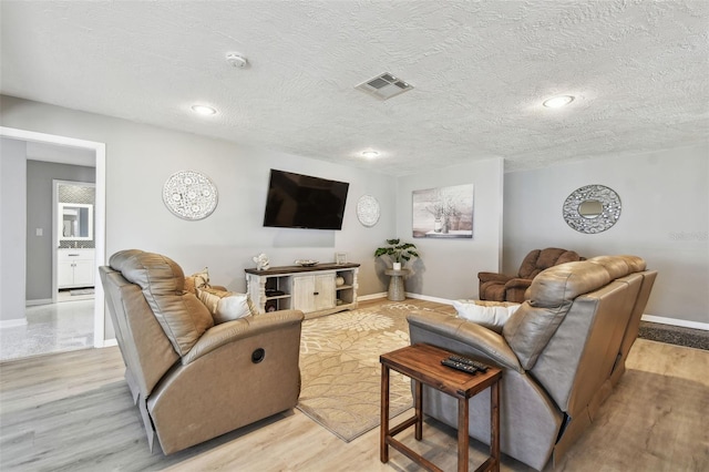 living room featuring baseboards, visible vents, a textured ceiling, and light wood finished floors