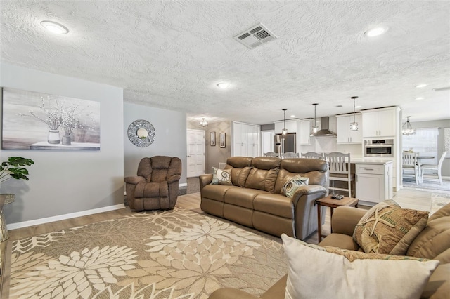 living area with a textured ceiling, recessed lighting, visible vents, baseboards, and light wood finished floors