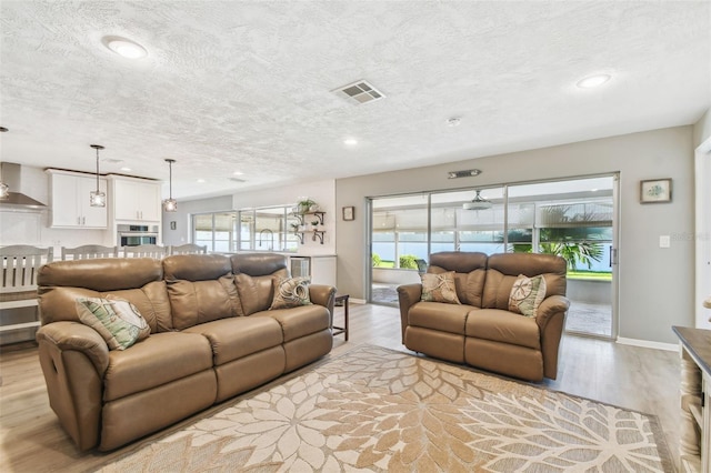 living room with light wood-style flooring, visible vents, and a healthy amount of sunlight