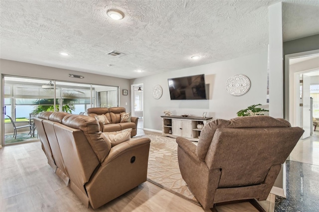 living room with a textured ceiling, light wood finished floors, visible vents, and baseboards