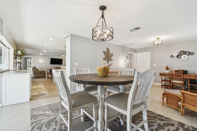 dining space with light speckled floor, a textured ceiling, visible vents, baseboards, and an inviting chandelier