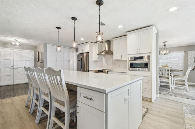 kitchen featuring stainless steel appliances, light wood-style floors, light countertops, a center island, and wall chimney exhaust hood