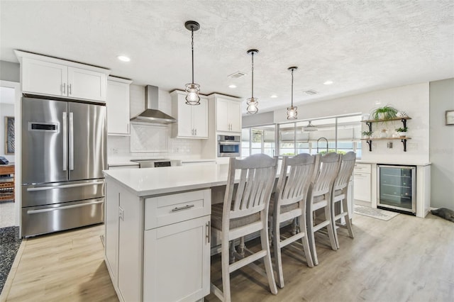 kitchen with wine cooler, a center island, backsplash, appliances with stainless steel finishes, and wall chimney range hood