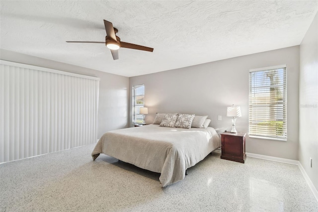 bedroom with a textured ceiling, speckled floor, a ceiling fan, and baseboards