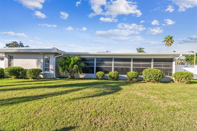 back of property with a yard, a tile roof, a sunroom, and stucco siding