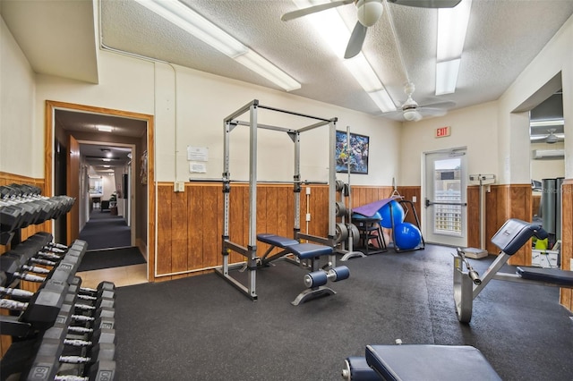 gym with a wainscoted wall, ceiling fan, and a textured ceiling