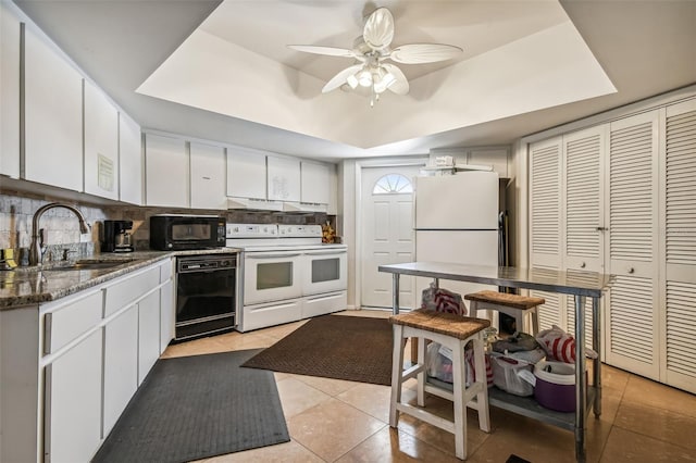 kitchen with a sink, a tray ceiling, black appliances, white cabinetry, and backsplash