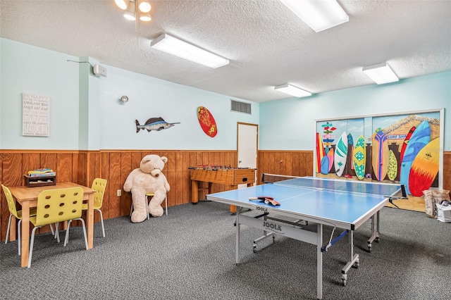 recreation room with wainscoting, visible vents, wood walls, and a textured ceiling