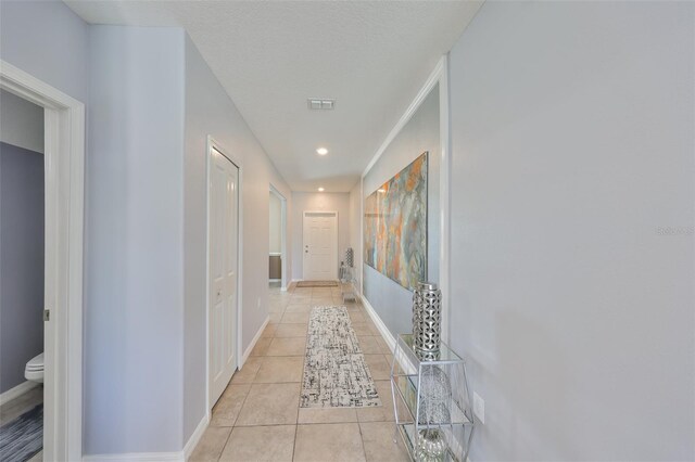 hallway featuring a textured ceiling, light tile patterned flooring, visible vents, and baseboards