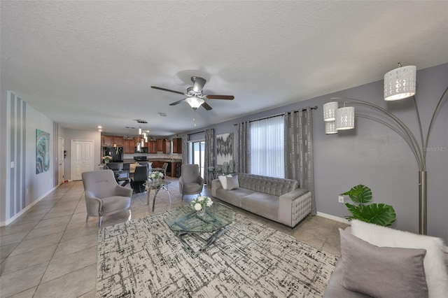 living room with a ceiling fan, a textured ceiling, baseboards, and light tile patterned floors