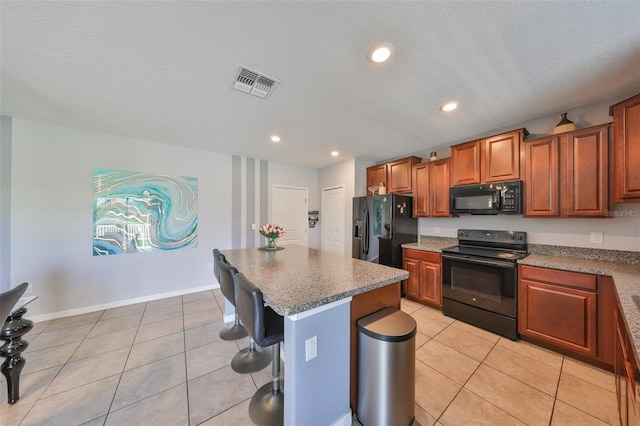 kitchen featuring light tile patterned floors, visible vents, a kitchen island, a kitchen breakfast bar, and black appliances