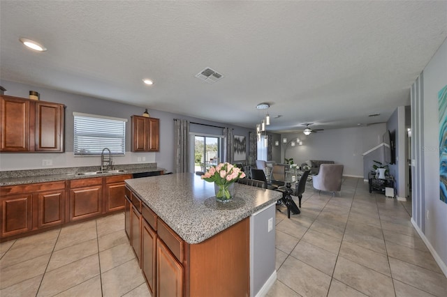 kitchen featuring visible vents, a kitchen island, open floor plan, stone counters, and a sink