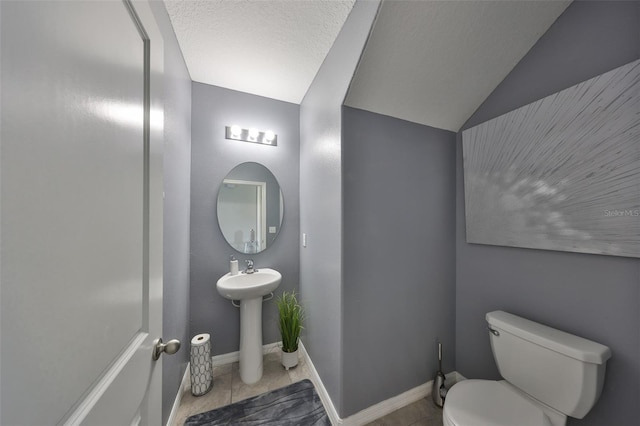 half bathroom featuring vaulted ceiling, toilet, baseboards, and tile patterned floors