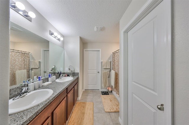 bathroom with a textured ceiling, double vanity, a sink, and tile patterned floors