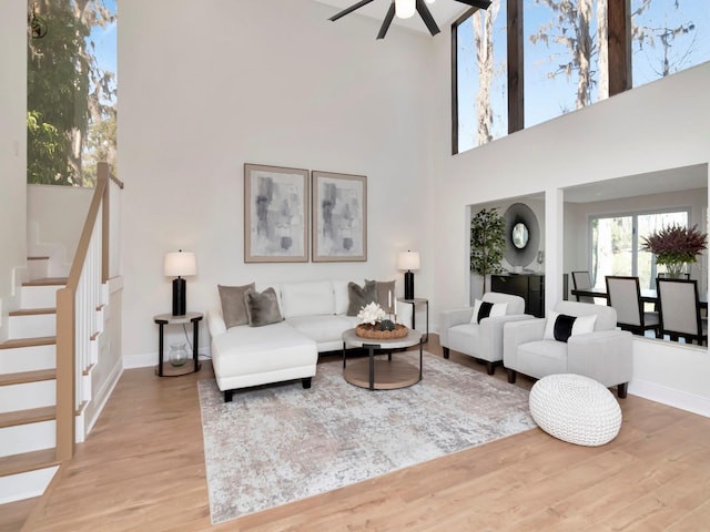 living room featuring ceiling fan, a high ceiling, wood finished floors, baseboards, and stairway