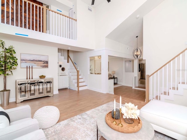 living room featuring a chandelier, wood finished floors, a towering ceiling, visible vents, and stairway