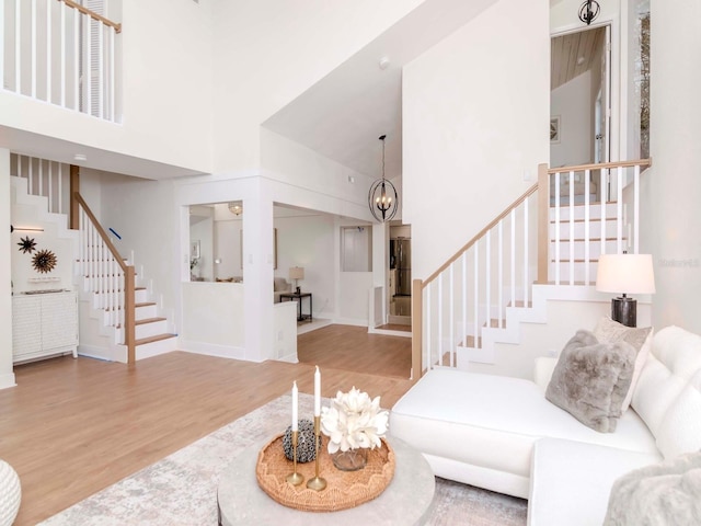 living area featuring stairs, wood finished floors, a towering ceiling, and an inviting chandelier