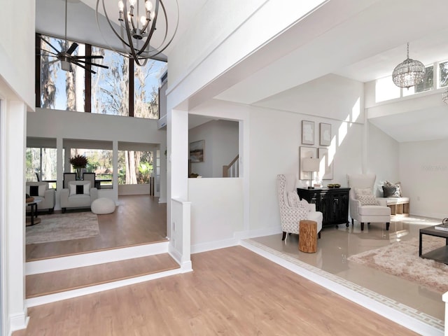 entryway featuring ceiling fan with notable chandelier, wood finished floors, a towering ceiling, baseboards, and stairway