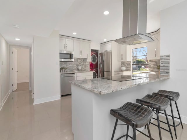 kitchen featuring a kitchen breakfast bar, a peninsula, island exhaust hood, stainless steel appliances, and white cabinetry