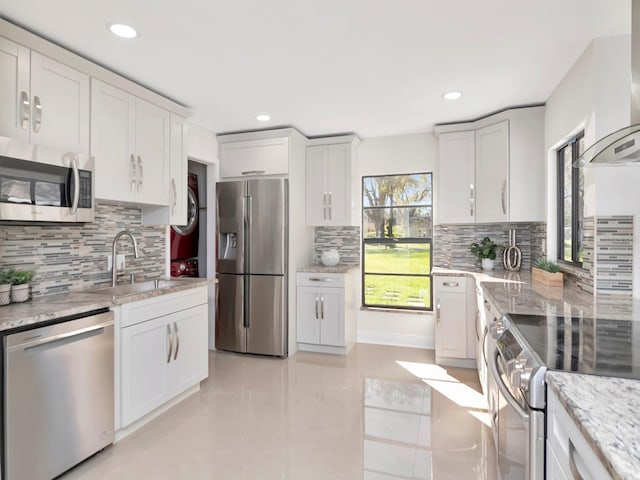 kitchen with light stone counters, extractor fan, stainless steel appliances, a sink, and white cabinetry