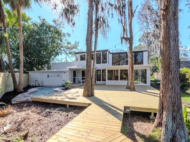 back of property with a sunroom, fence, a deck, and stucco siding