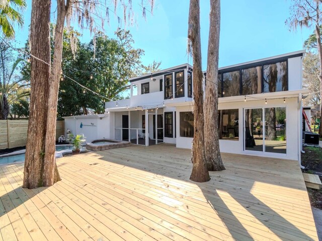 rear view of property featuring fence, stucco siding, a wooden deck, and a hot tub