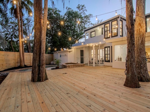 rear view of property with a hot tub, fence, a deck, and stucco siding