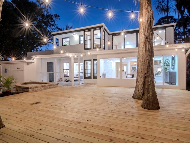 back of house at twilight with a hot tub, a wooden deck, and stucco siding