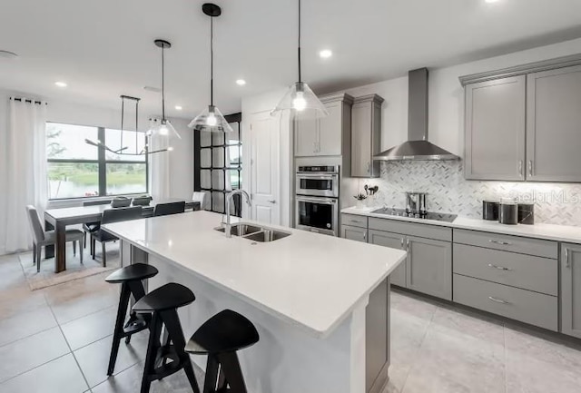 kitchen featuring stainless steel double oven, black electric stovetop, a sink, gray cabinetry, and wall chimney range hood