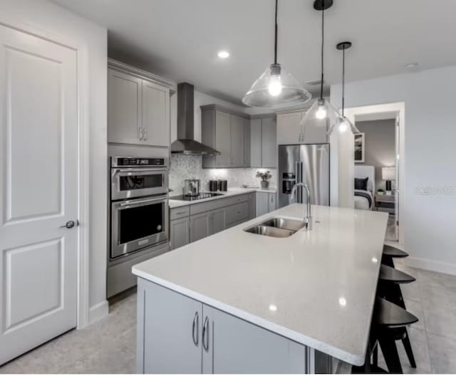 kitchen with appliances with stainless steel finishes, gray cabinetry, wall chimney range hood, and a sink