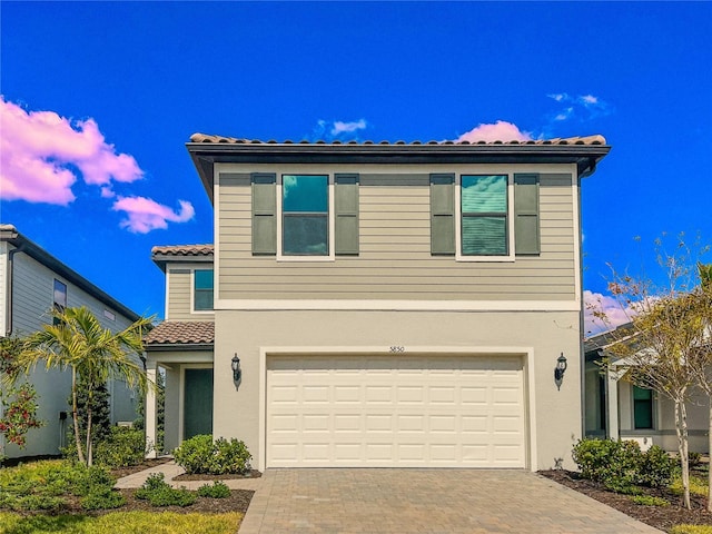 view of front of home with a tile roof, decorative driveway, a garage, and stucco siding