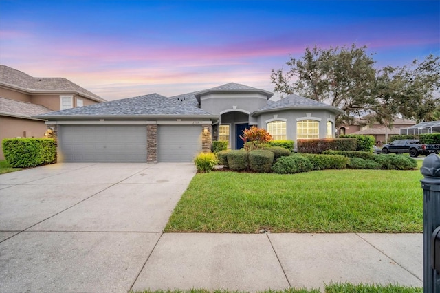 view of front of home with stucco siding, a front yard, a garage, stone siding, and driveway