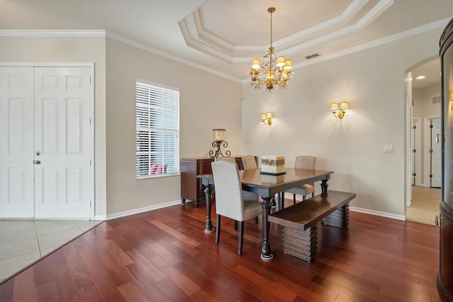 dining area with arched walkways, a raised ceiling, wood finished floors, and ornamental molding