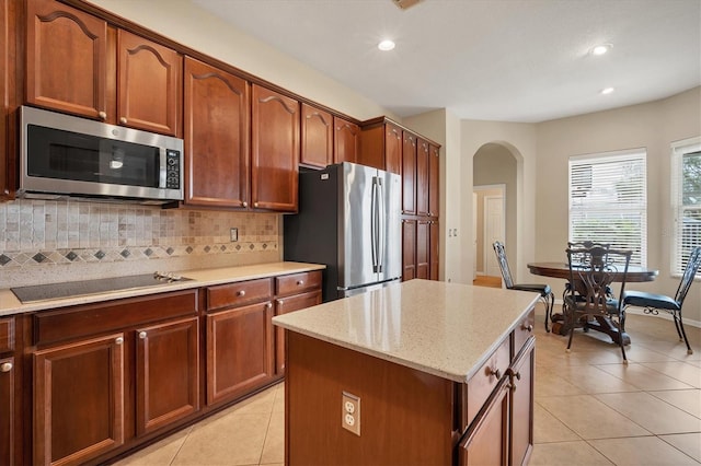 kitchen featuring arched walkways, stainless steel appliances, light tile patterned floors, and backsplash