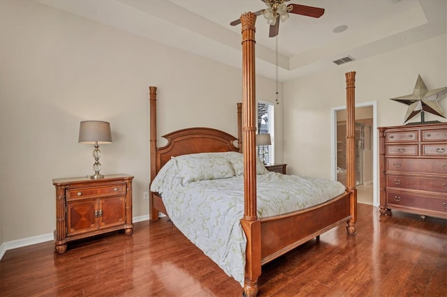 bedroom featuring baseboards, visible vents, dark wood-type flooring, and a tray ceiling