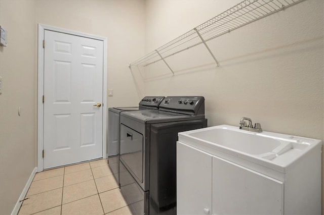 washroom featuring light tile patterned floors, laundry area, a sink, baseboards, and washing machine and clothes dryer