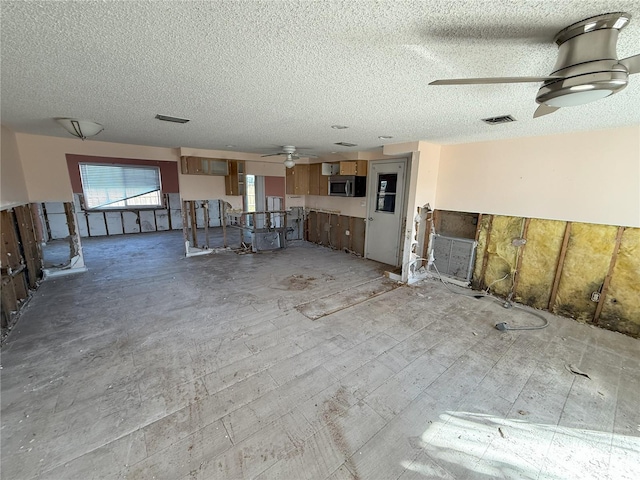 unfurnished living room with a ceiling fan, visible vents, and a textured ceiling