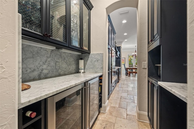 kitchen with arched walkways, dark cabinets, beverage cooler, decorative backsplash, and stone tile flooring