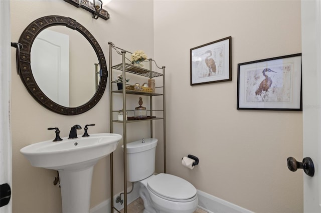 half bath with baseboards, a sink, and toilet