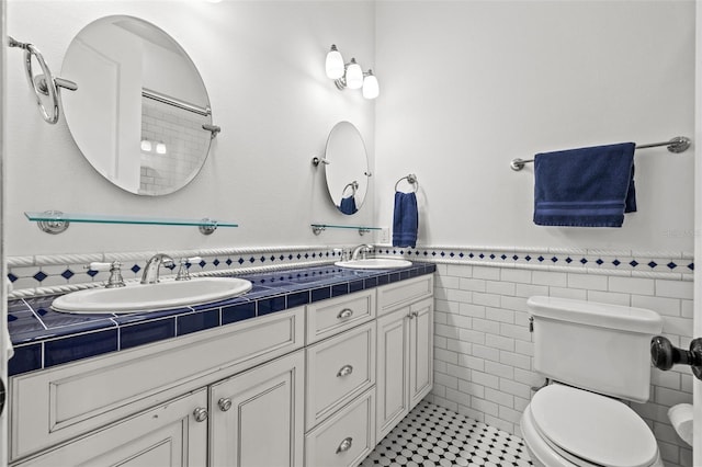 full bath with a wainscoted wall, double vanity, a sink, and toilet