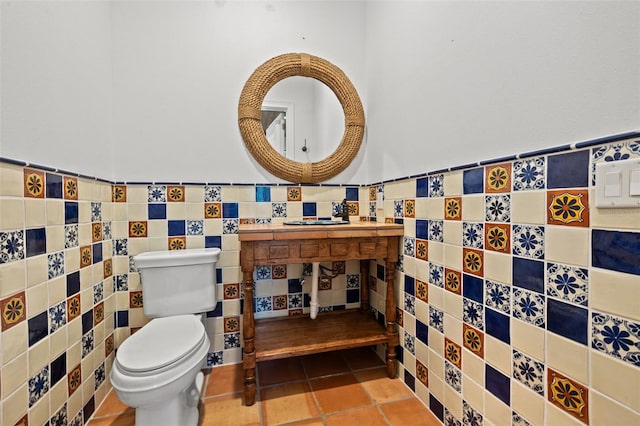 half bathroom with toilet, tile patterned floors, tile walls, and wainscoting