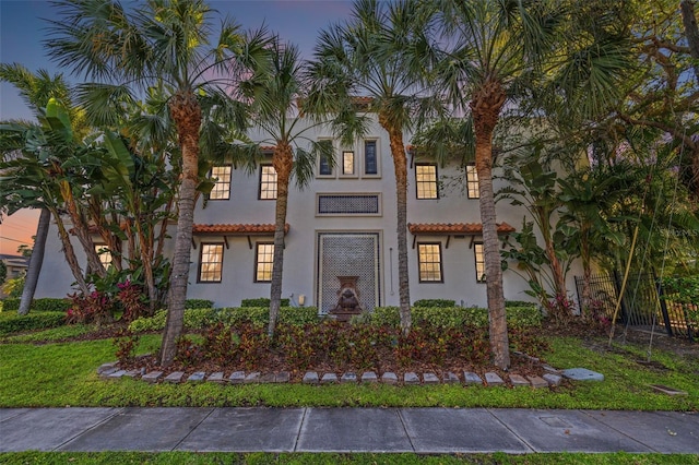 mediterranean / spanish house with a tiled roof, fence, and stucco siding