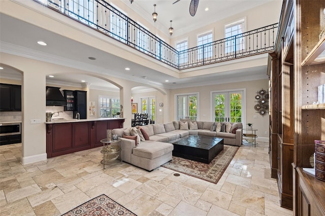 living area with baseboards, a towering ceiling, ornamental molding, stone tile flooring, and recessed lighting